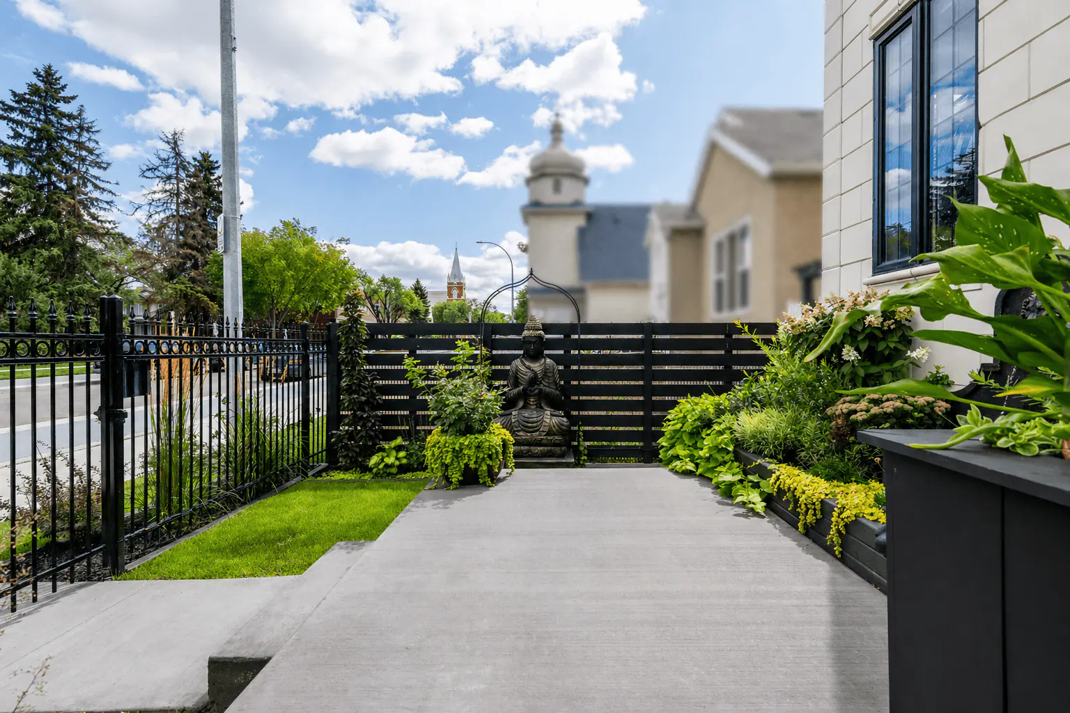 Front entrance garden with black fencing, statue, concrete levels, and layered planting by Interiors on Main